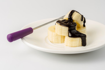 Sliced ​​bananas in chocolate icing on a white saucer with a fork of fondue