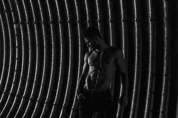 Muscular young man with beard on dark tunnel urban background. Fashion portrait of brutal strong muscle guy with modern trendy hairstyle. Model, fashion concept. Sexy naked torso. Black and white.