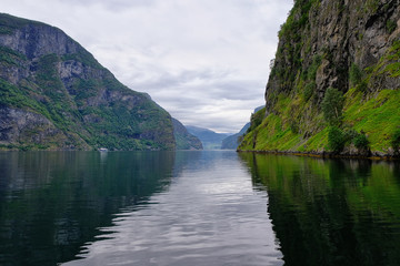 Fototapeta premium Holy grail illustrated from Sognefjord or Sognefjorden created from mountain range with blue sky and reflection in clear water and having a wooden dock point out in a river in Flåm