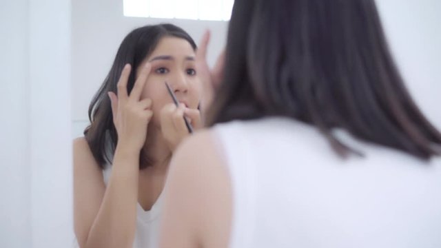 Beautiful Asian woman using eyeshadow make up in front mirror, Happy female using beauty cosmetics to improve herself ready to working in bedroom at home. Lifestyle women relax at home concept.