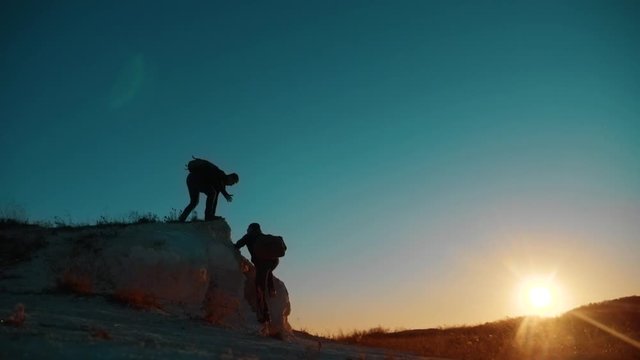 Teamwork tourists. friendship hiking help each other trust assistance silhouette in mountains. Backpacker helps to his friend to climb to rock. two travelers help stretching hand. tourist victory