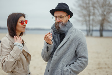 Young attractive girl and man walk along a deserted sandy beach. Romantic mood. Couple in love. Street shot.