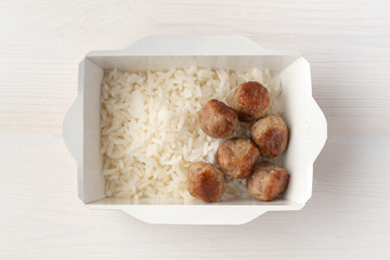 Cooked rice and meatballs in paper lunch box on wooden background