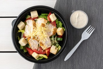 Caesar salad in round black lunchbox on wooden background