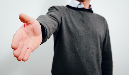 Holding out a hand in front of a man. A man wearing a gray sweater stretches out a helping hand, greeting or saying goodbye. Greetings concept.