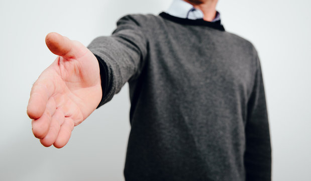 Holding Out A Hand In Front Of A Man. A Man Wearing A Gray Sweater Stretches Out A Helping Hand, Greeting Or Saying Goodbye. Greetings Concept.