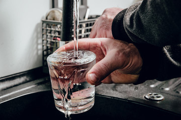 Pouring water into a glass. Man pours water from a black tap into a transparent glass. The concept of saving water, problems with water, lack of water in various regions of the world.