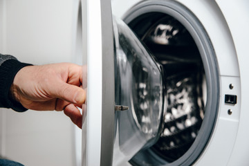Opening the door from the washing machine. The man opens the door from the washing machine to put on dirty clothes. The concept of doing laundry.