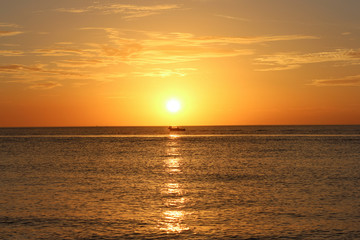 Fototapeta na wymiar Boat in Orange Sunset, Boat with people sitting on bow centered under sunset, Gorgeous Florida Sunset