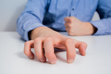 A man dressed in a blue shirt has his hands folded on the table. The businessman nervously holds...