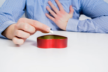 A businessman dressed in a blue checkered shirt is holding his heart and takes out a pill for the heart. Problems of people at work, work-related stress. Myocardial infarction, disease prevention.