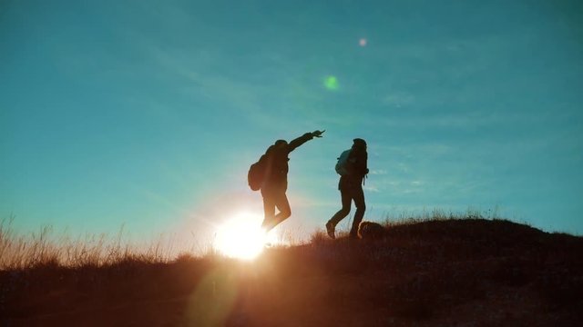 teamwork. Two hikers enjoying sunrise from top of a mountain and dog. Two hikers with backpacks climbing a peak on cloud sky background and dog. hikers lifestyle adventure and the dog go walking