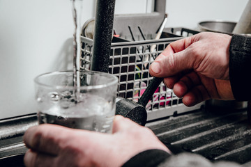 Pouring water into a glass. Man pours water from a black tap into a transparent glass. The concept of saving water, problems with water, lack of water in various regions of the world.