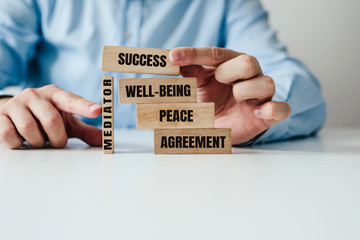The role of the mediator in maintaining stability in life. Man arranges wooden blocks with inscription PEACE, AGREEMENT supported by a wooden MEDIATOR block. Role of mediation in maintaining order. - obrazy, fototapety, plakaty
