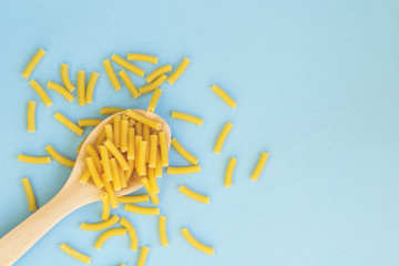 Raw pasta in the wooden spoon on blue background.