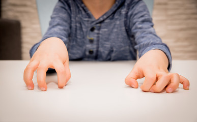 The nervousness of a little boy. The child nervously and impatiently holds his hands on the table....