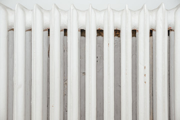 View of an old white finned radiator. An old cast iron radiator that warms the room. The concept of heating the apartment in cold days, convector with water.