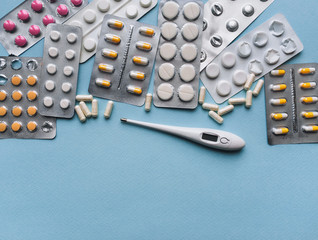 A variety of colored pills and electronic thermometer lie on a blue background. Modern medicine and...