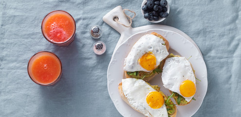 banner of avocado sandwich and fried egg with paprika on the table. healthy breakfast or snack on a plate on a blue linen tablecloth and freshly squeezed grapefruit juice