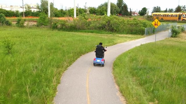 Disabled person driving a motorized mobility scooter for elderly and or disabled. Recreational electric ability vehicle for handicapped footage movement from behind aerial. Accessibility concept.