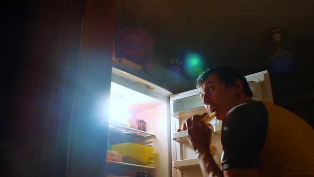 man eats hunger and gluttony from the refrigerator at night. man looks into the fridge at night. gluttony overweight lifestyle overeating concept