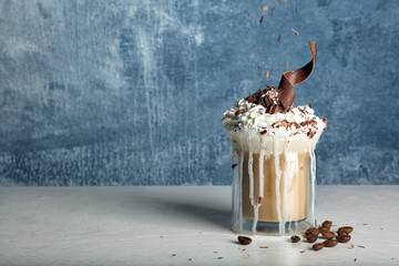 Glass cup of tasty coffee with whipped cream and chocolate on table against color background. Space...
