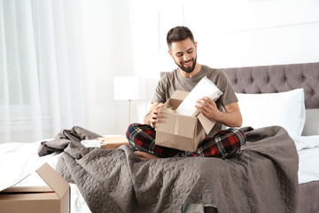 Young man opening parcel in bedroom at home
