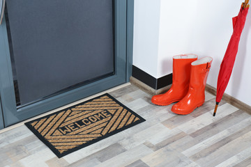 Rubber boots, umbrella and mat near door in hallway