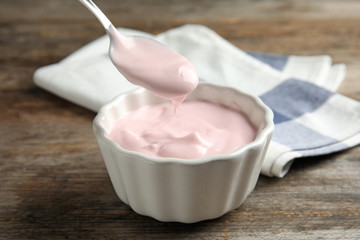 Spoon with creamy yogurt over bowl on wooden table