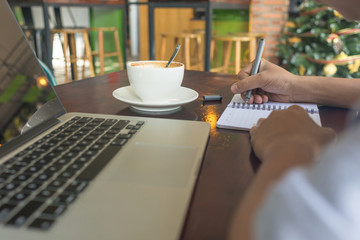 Human hand writing notes with the cup of coffee beside