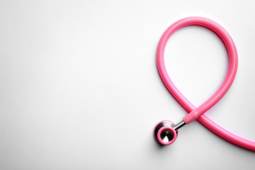 Pink stethoscope folded like awareness ribbon on white background, top view with space for text. Breast cancer concept