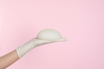 Doctor holding silicone implant for breast augmentation on color background, space for text....