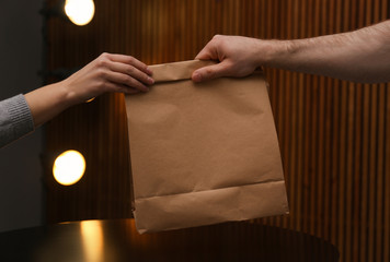 Man giving paper bag with order to customer in cafe, closeup. Mock up for design