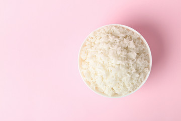Bowl of boiled rice on color background, top view with space for text