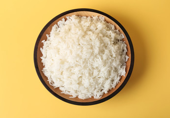 Bowl of boiled rice on color background, top view