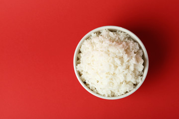Bowl of boiled rice on color background, top view with space for text