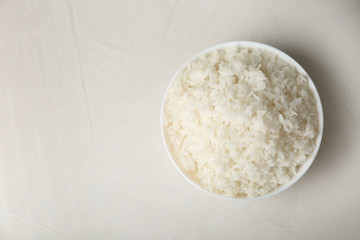 Bowl of boiled rice on light background, top view with space for text