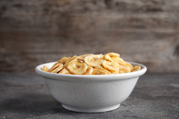 Bowl with sweet banana slices on grey table, space for text. Dried fruit as healthy snack