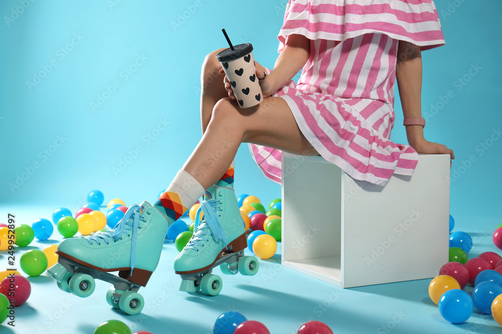 Wall mural Young woman with retro roller skates and cup of drink on color background, closeup. Space for text