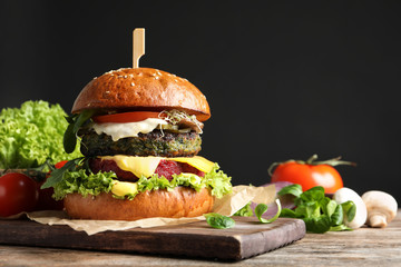 Vegan burger and vegetables on table against dark background. Space for text