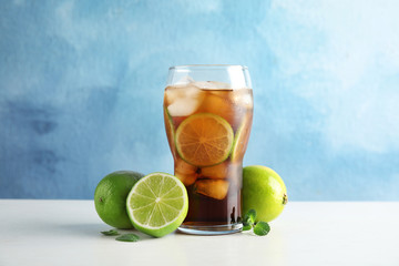 Glass of coke with ice cubes and limes on table against color background