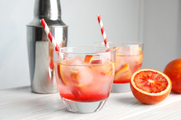 Glass of tropical cocktail with ice cubes on table against light background