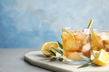 Glass of lemonade with ice cubes and fruit on table against color background. Space for text