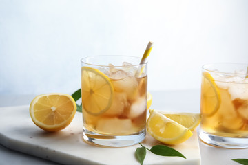 Glasses of lemonade with ice cubes and fruit on table against color background