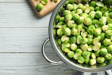 Colander with Brussels sprouts on wooden background, top view. Space for text