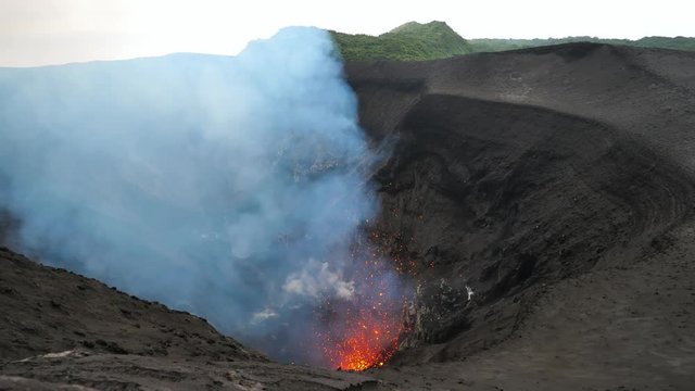 Stunning shot of an active volcano spewing out glowing lava high in the air. Mount Yasur exploding and belching out hot pieces of magma. Dark clouds of smoke rise from the base of the deep crater.
