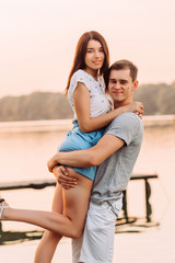 Loving young couple hugging on pier at sunset in summer.