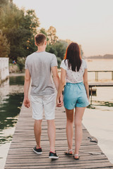 Loving young couple walking on pier at sunset in summer.