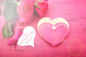 International Women's Day heart shape cookies decorated as pink ladies dresses with bouquet of pink roses on vintage pink wood with lens flare
