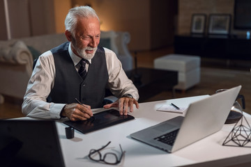Happy mature editor using digitized pen while working on computer in his office.